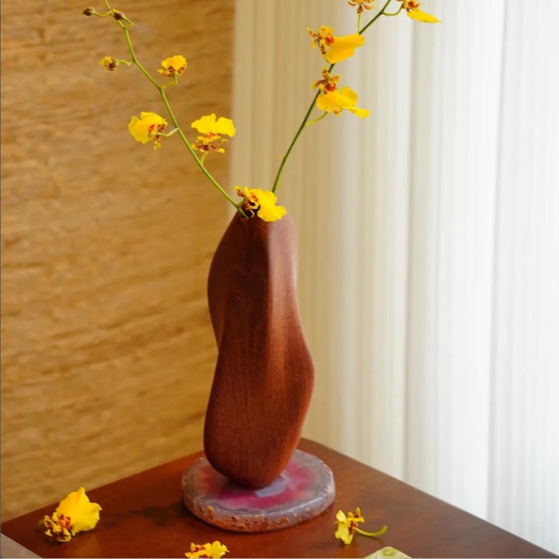 Handcarved wooden bud vase holding yellow orchid stems, used as decor on an indoor living room table (wall+ curtain backdrop)