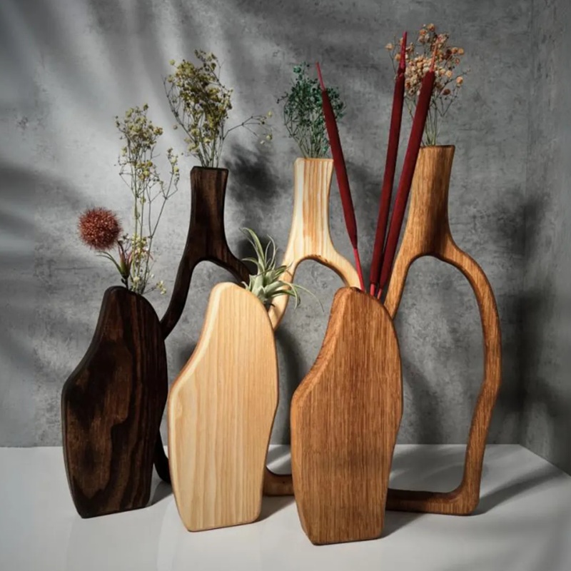 Assorted handcarved hollowed wooden vases set with dried florals, displayed on white surface against concrete background