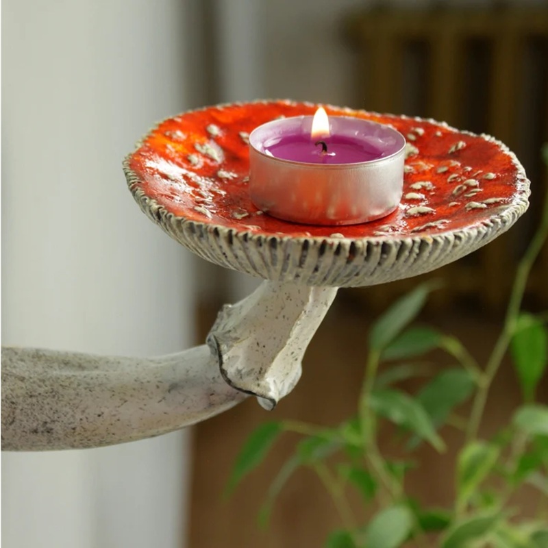 Close-up of red spotted toadstool ceramic wall candle holder with lit purple tealight—whimsical forest home decor