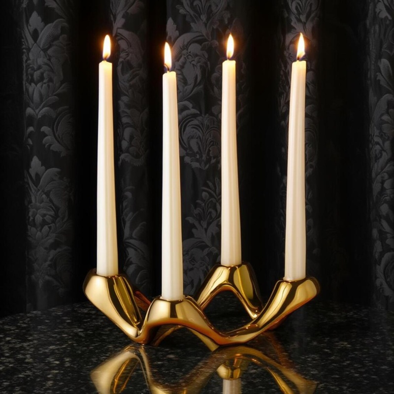 Polished gold metallic ceramic candelabra (modern curved frame) with lit straight taper candles, placed on black marble table